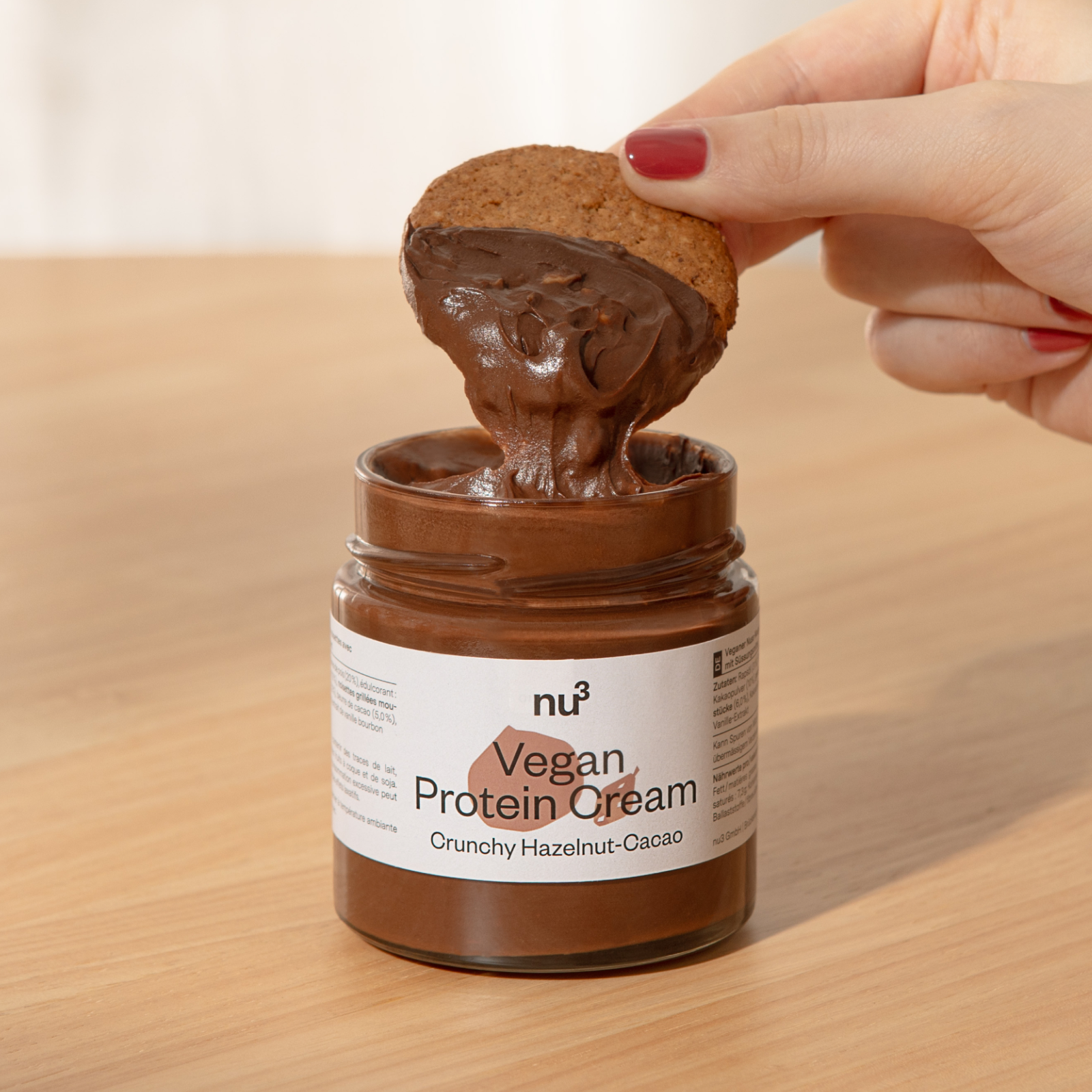 Hand tunkt Keks in ein Glas mit nu3 Vegan Protein Cream